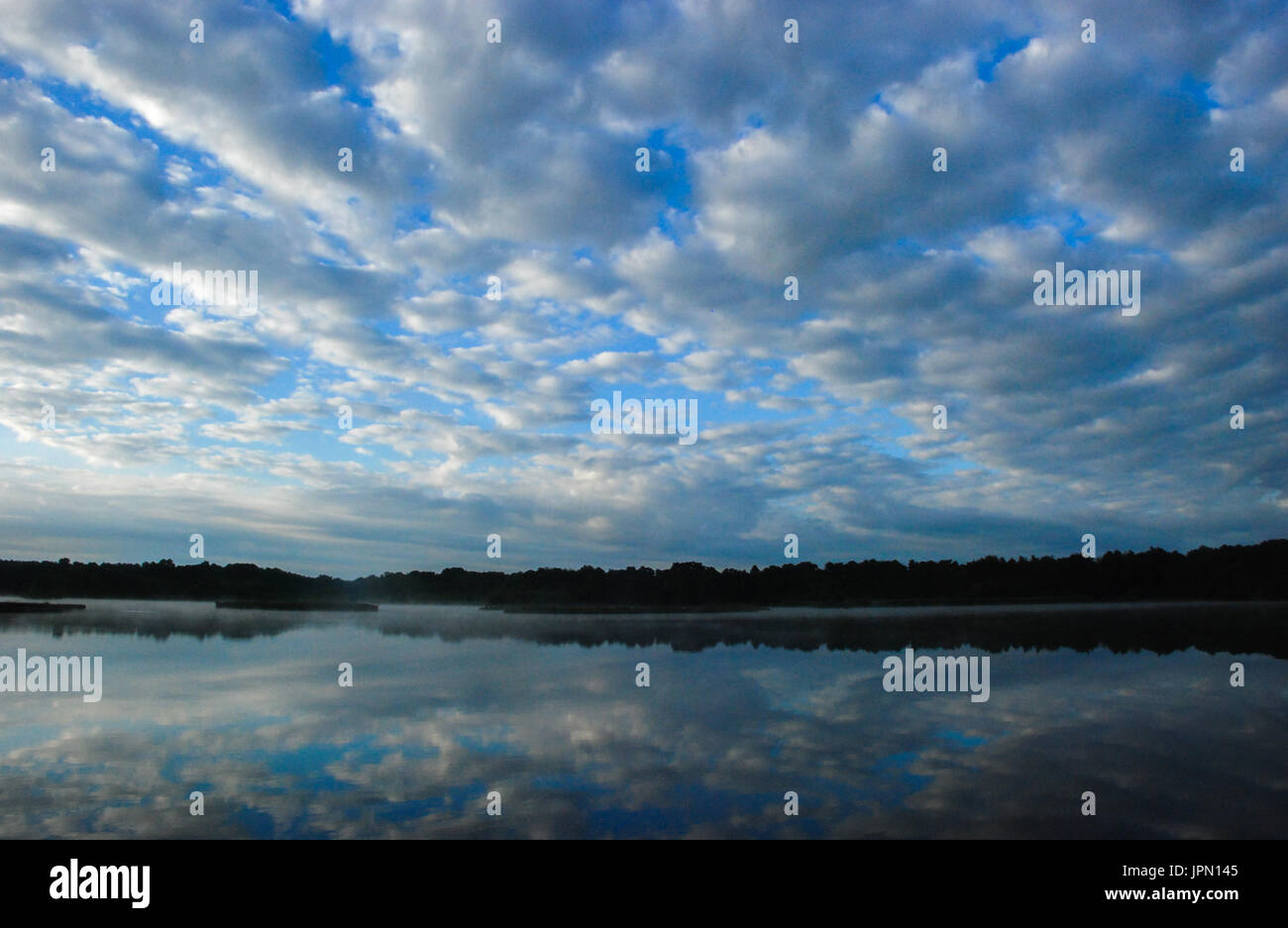 Early morning reflections of altocumulus clouds and blue sky in the water at Fleet Pond, Hampshire, UK Stock Photo