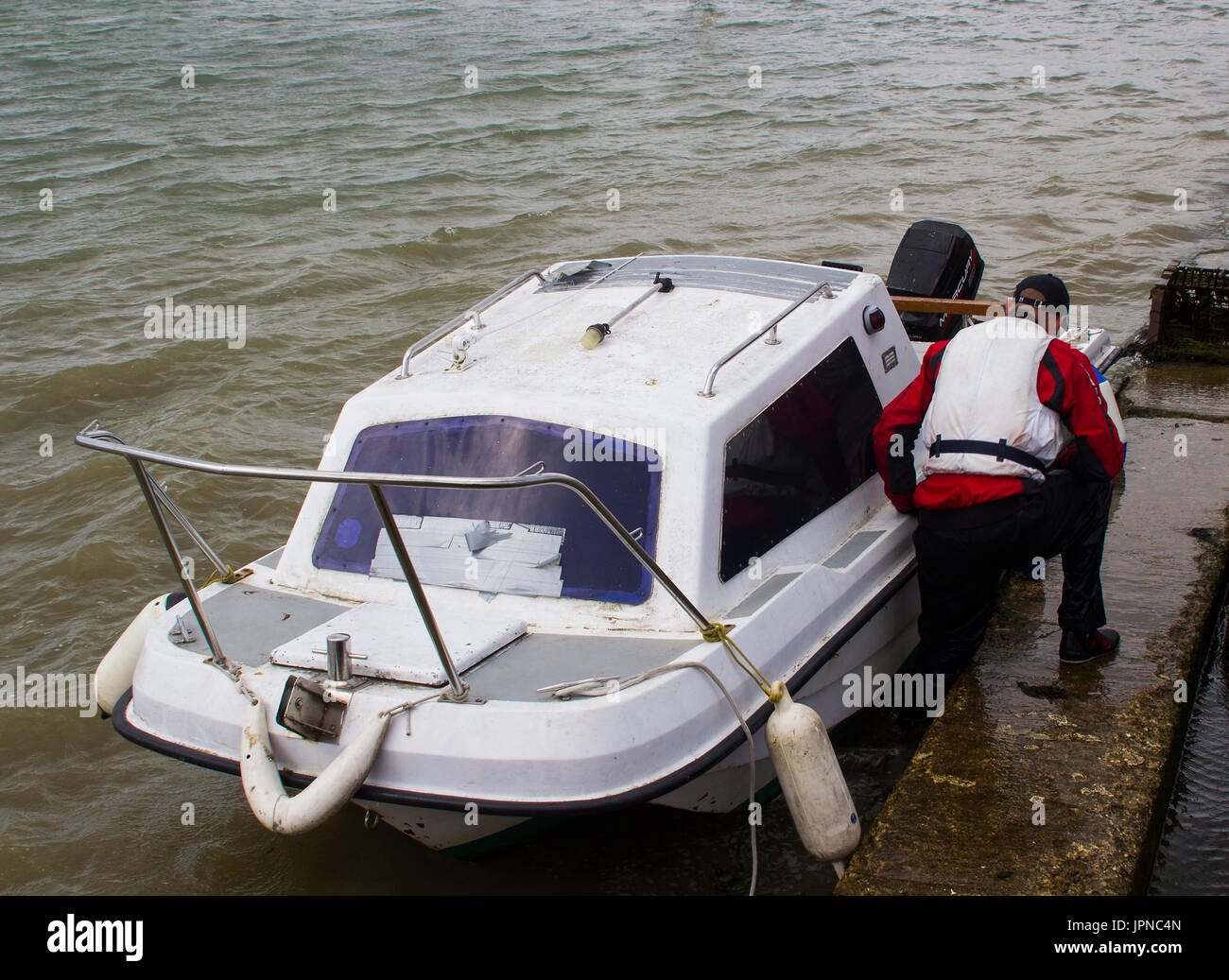 A boat owner bringing his small fibre glass boat toward the shore in Warsash, Hampshire to a waiting trailer in order to take it out of the water for Stock Photo