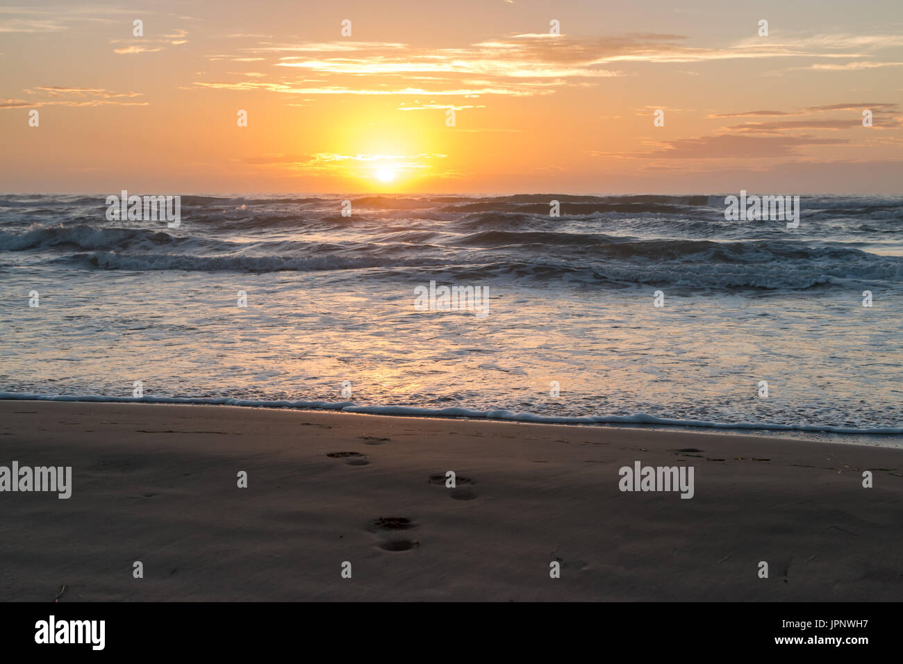 Sun Rising Over Calm Ocean with Foot Prints in the Foreground Stock Photo