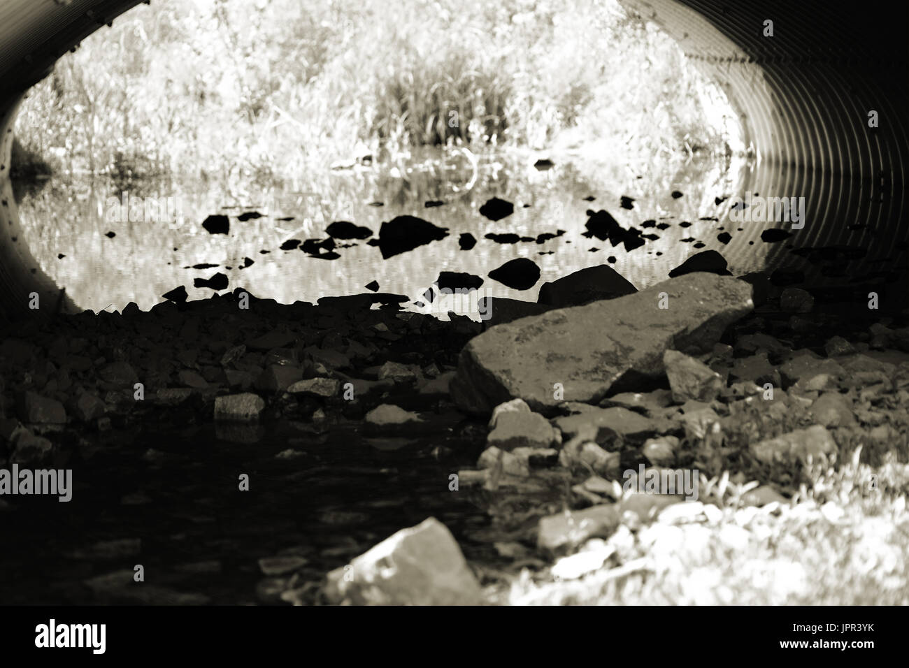 Water and the stones of a rubbish bed of a pond under a tubular bridge