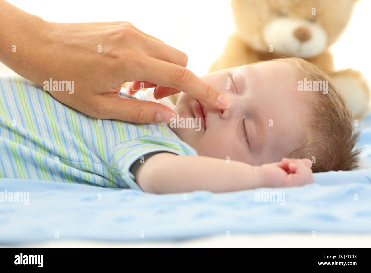 Mother hand touching the nose of a baby sleeping on a bed Stock Photo
