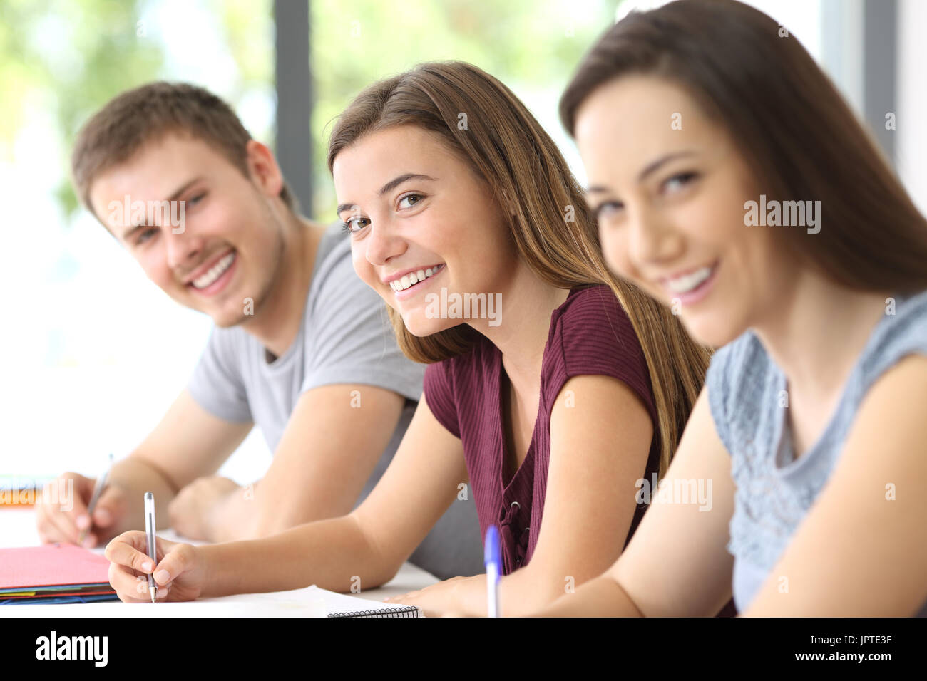 Three happy students looking at you in a classroom Stock Photo - Alamy