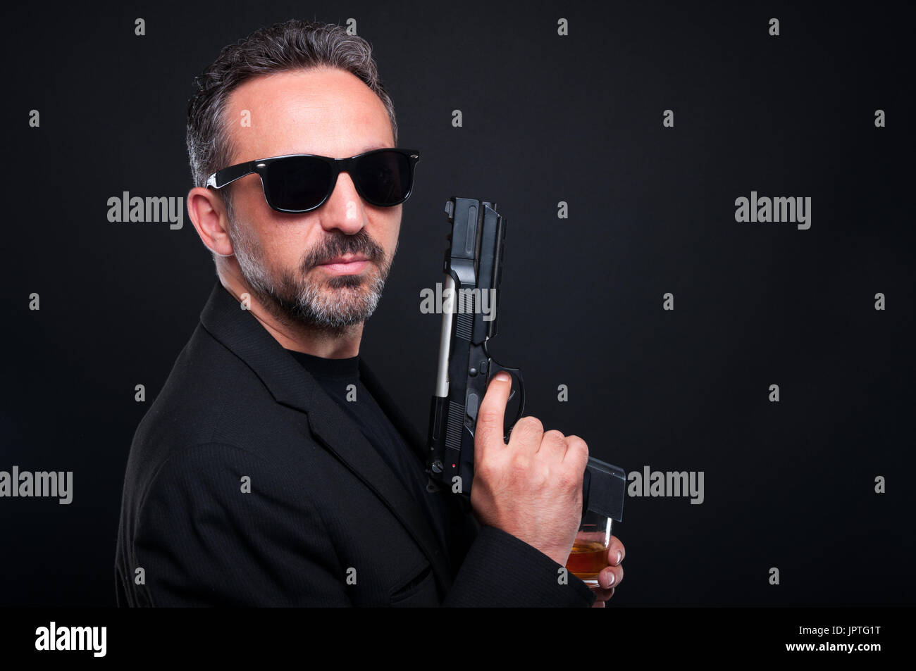 Mafia member holding a gun or pistol while drinking whiskey on black