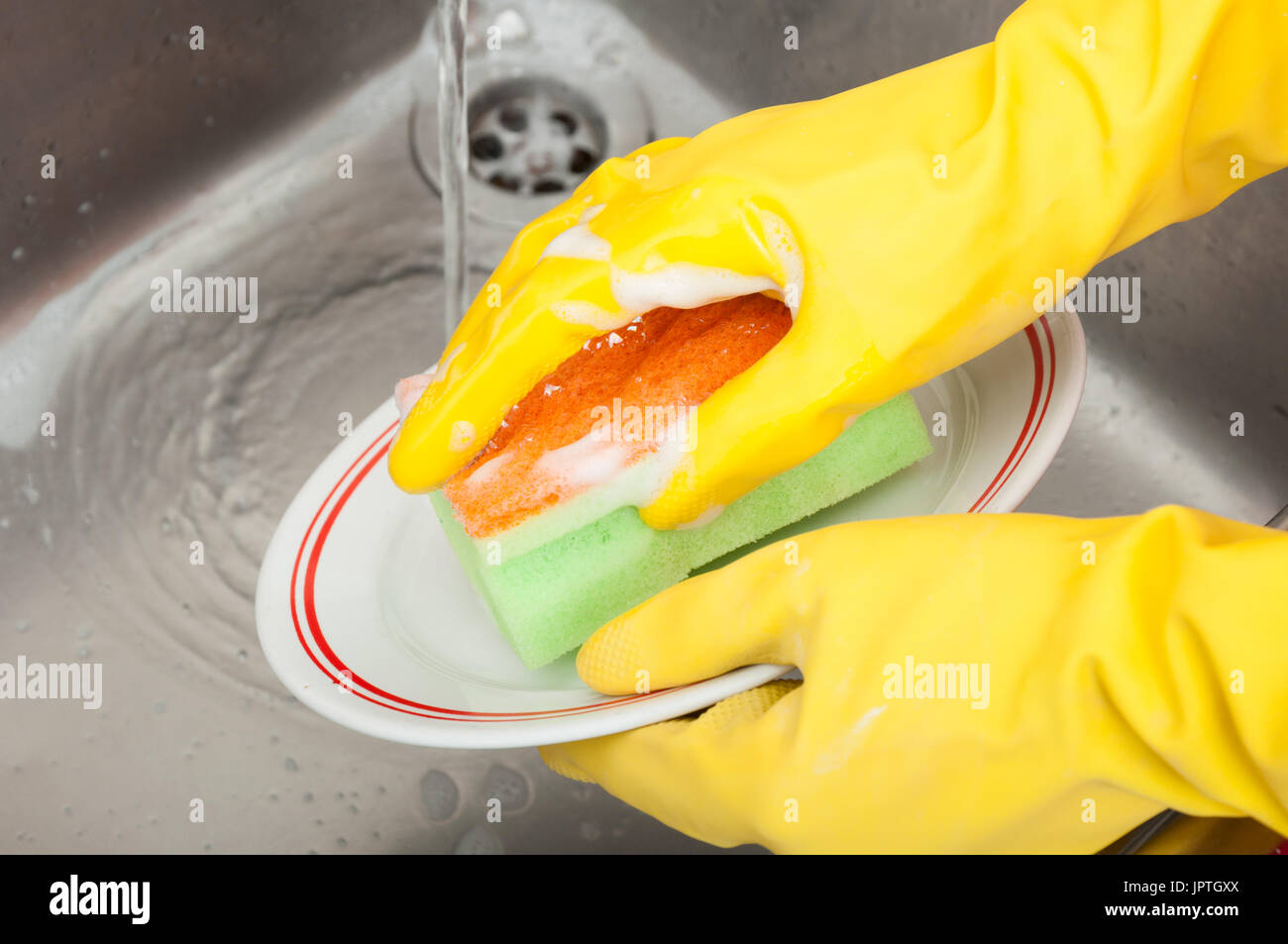 Cleaning lady or housewife with rubber gloves and sponge washing dish in close-up Stock Photo