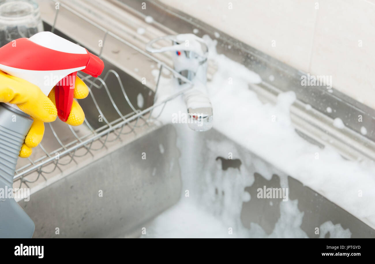 Woman washing the sink and tap with disinfecting spray in closeup Stock Photo