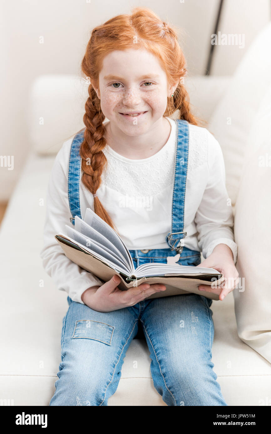 Adorable little girl holding book and smiling at camera Stock Photo - Alamy