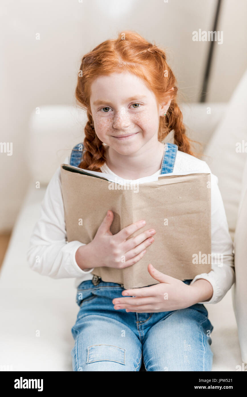 Adorable little girl holding book and smiling at camera Stock Photo - Alamy