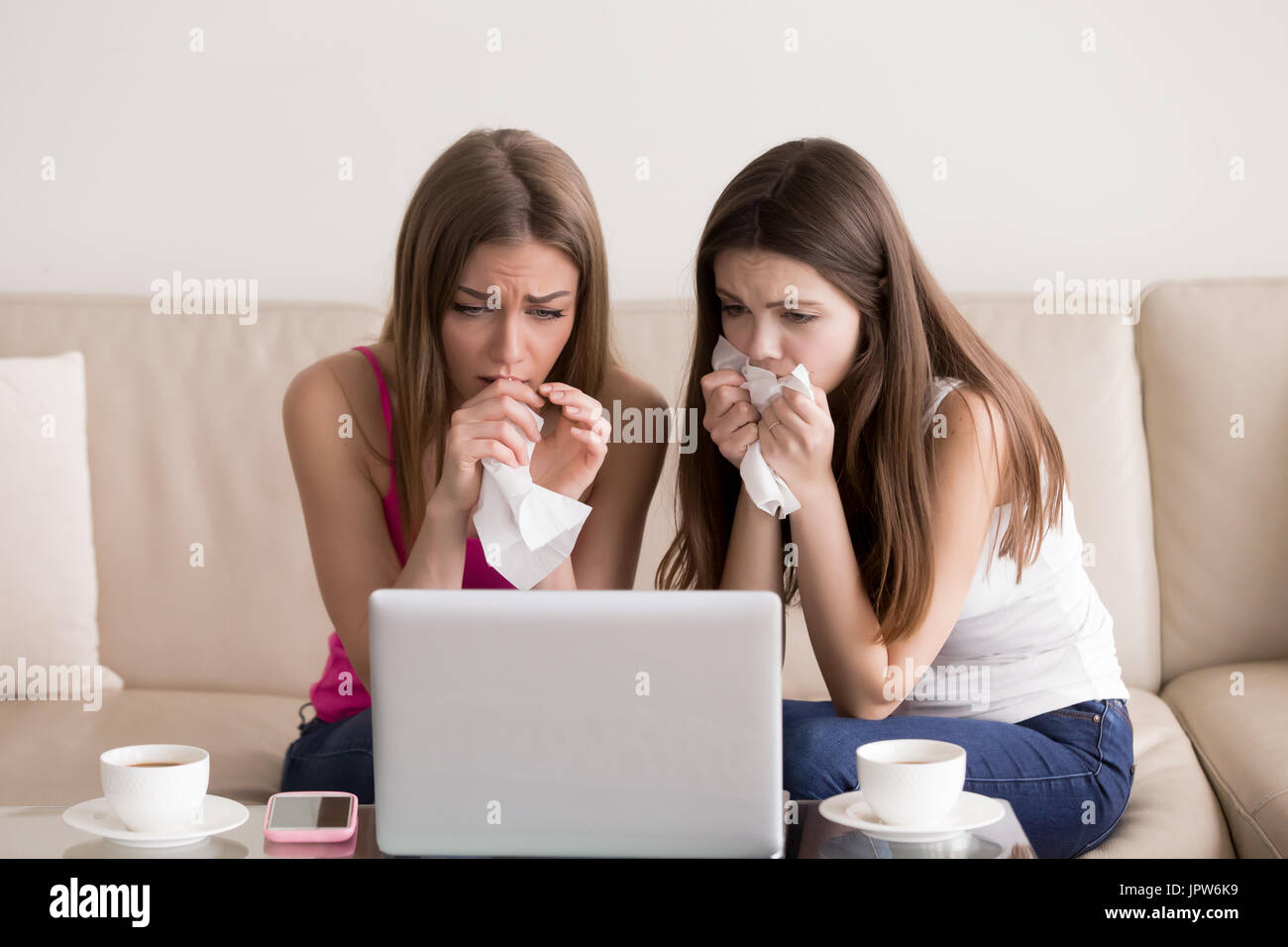 Two girlfriends crying while watching sad movie Stock Photo