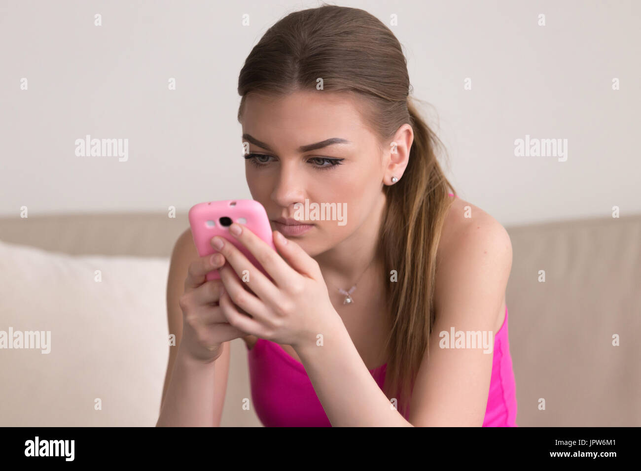 Serious young woman using cellphone at home Stock Photo