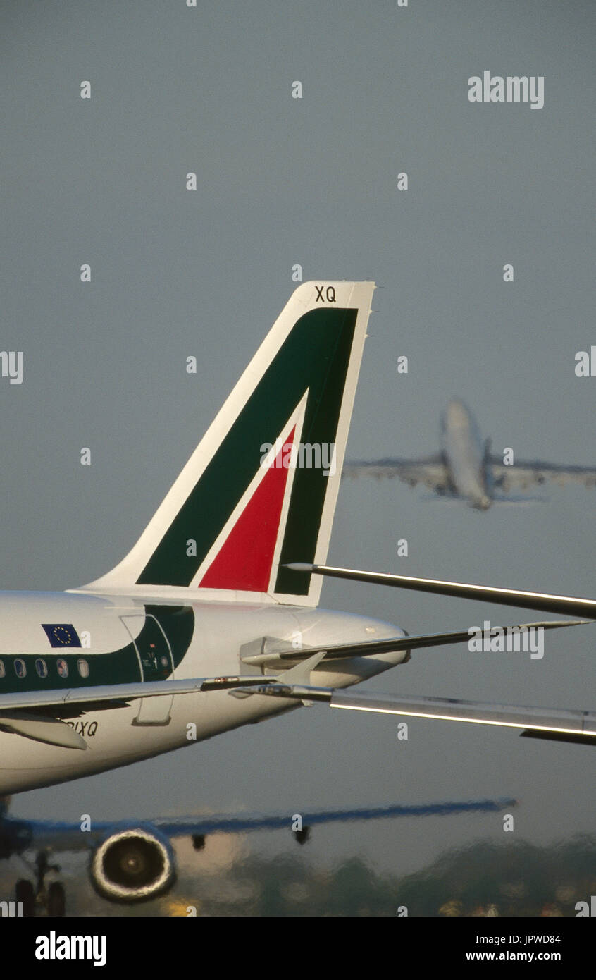 tail-fin of an Alitalia Airbus A321-100, wing and CFM56-3 jet-engine of a Boeing 737-300 taxiing and a Boeing 747 climbing out after take-off behind Stock Photo