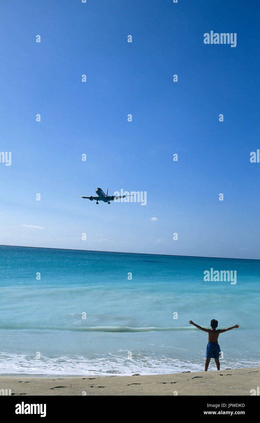 US Airways Boeing 757-200 on very low final-approach landing over Maho Beach with boy child standing on beach waving Stock Photo
