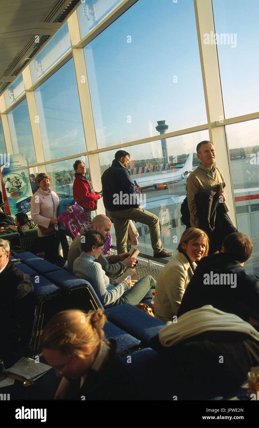passengers waiting in a full departure-lounge next to windows with an air-traffic control-tower and Boeing 737-300 behind Stock Photo