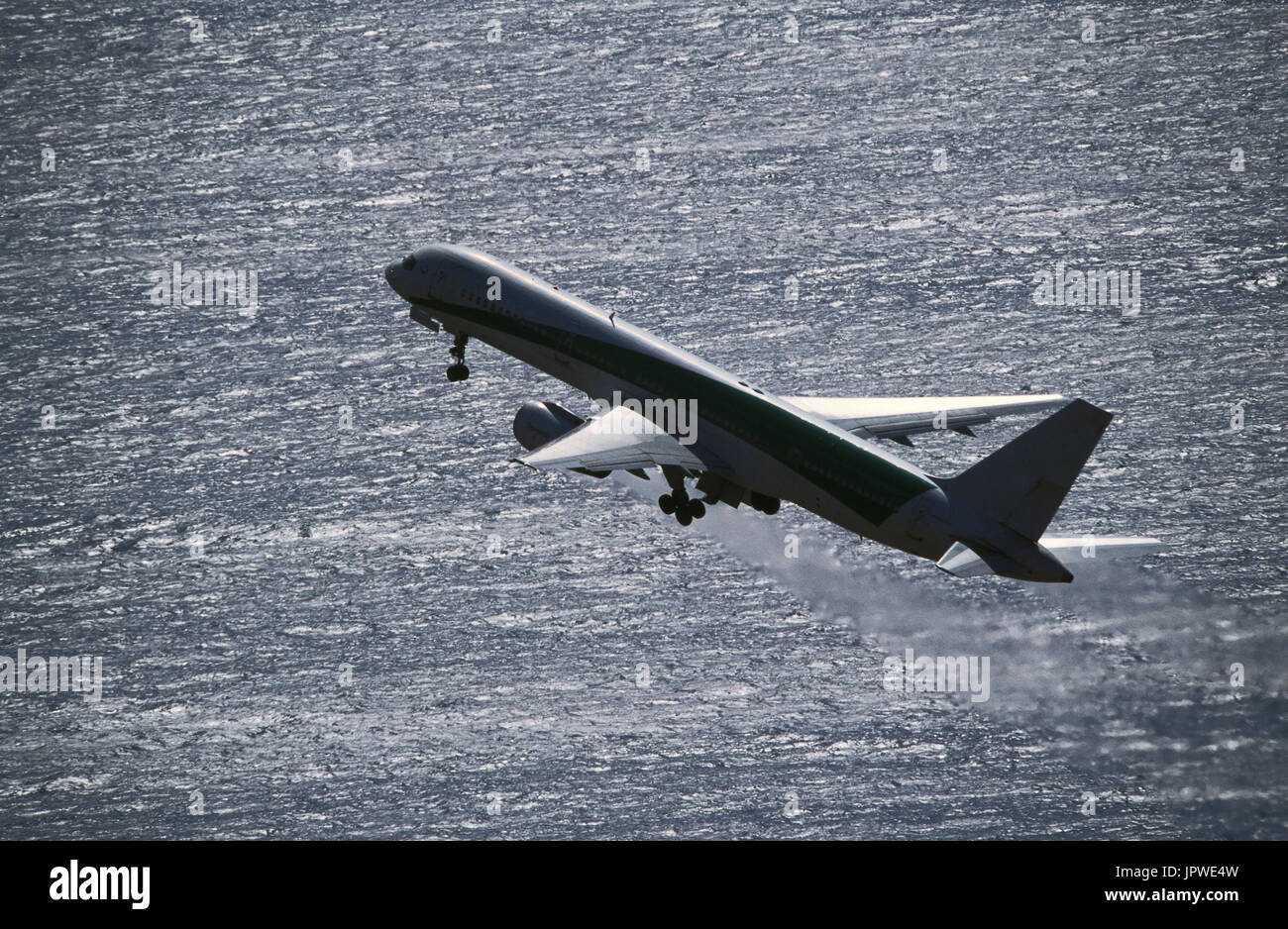 Boeing 757-200 climbing out after take-off over the sea with jet-exhaust visible from the engines and undercarriage retracting Stock Photo