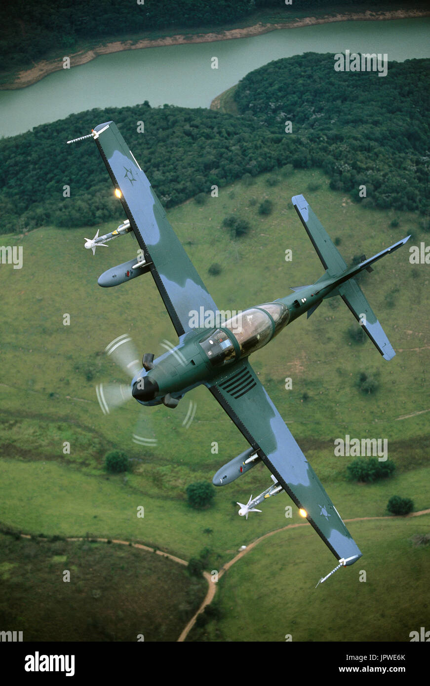 Brazilian Air Force Embraer EMB-314 Super Tucano banking over river, fields and trees Stock Photo