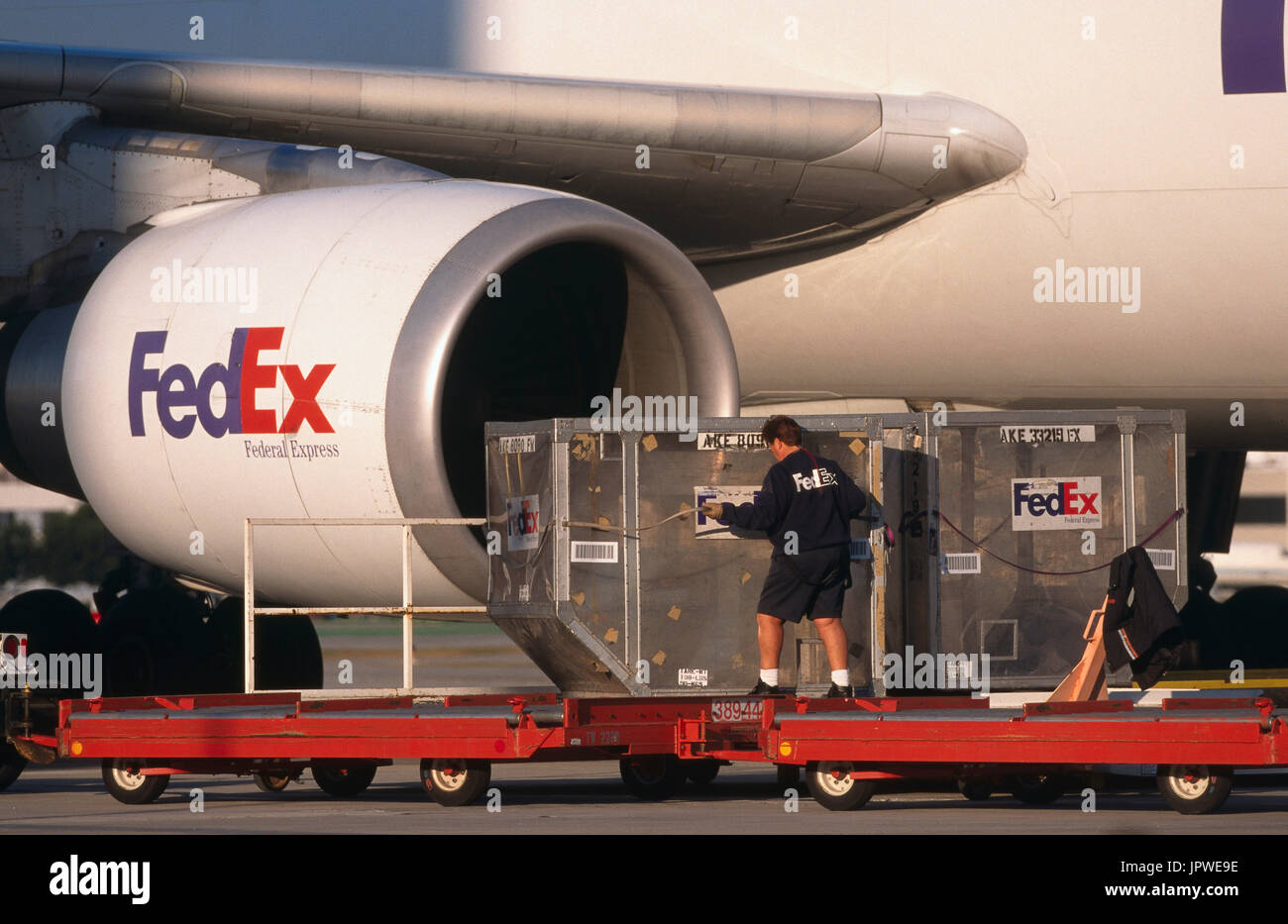 men moving LD3 containers on trolleys with CF6-80 engine-intake of a FedEx Airbus A300-600 freighter Stock Photo