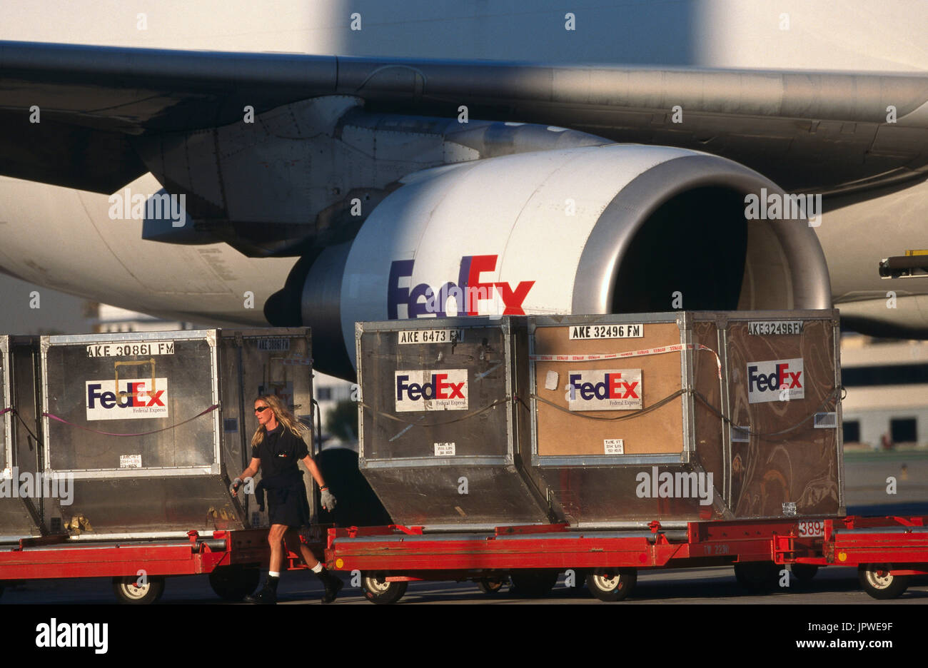 LD3 containers being loaded onto trolleys with a GE CF6-80 engine-intake of a FedEx Airbus A300-600 freighter behind Stock Photo