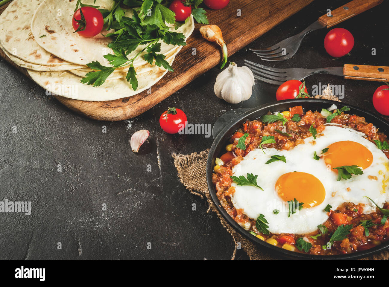 Traditional Mexican dish Huevos rancheros - scrambled eggs with tomato salsa, with taco tortillas, fresh vegetables and parsley. Breakfast for two. On Stock Photo