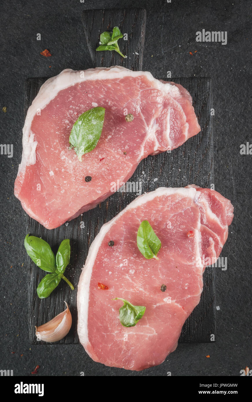 Raw organic meat. Pork steaks, fillets for grilling, baking or frying. On a wooden cutting board, with salt, pepper, basil, tomatoes, garlic. On a gra Stock Photo