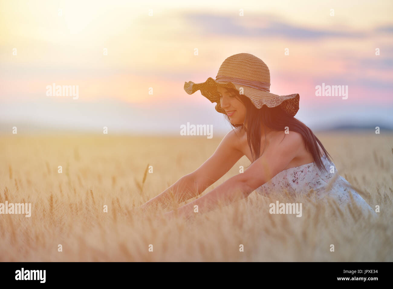 Closeup portrait of smiling young caucasian woman in nature. Cheerful young beautiful woman touching wheat field at sunset Stock Photo