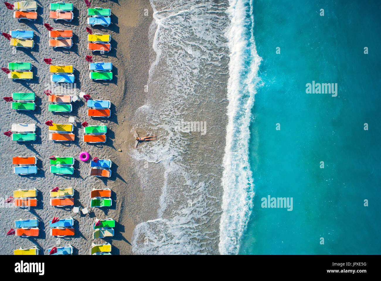 Beautiful young woman on the sea at sunrise in Oludeniz, Turkey. Aerial view of lying woman on the beach with colorful chaise-lounges. Top view from d Stock Photo