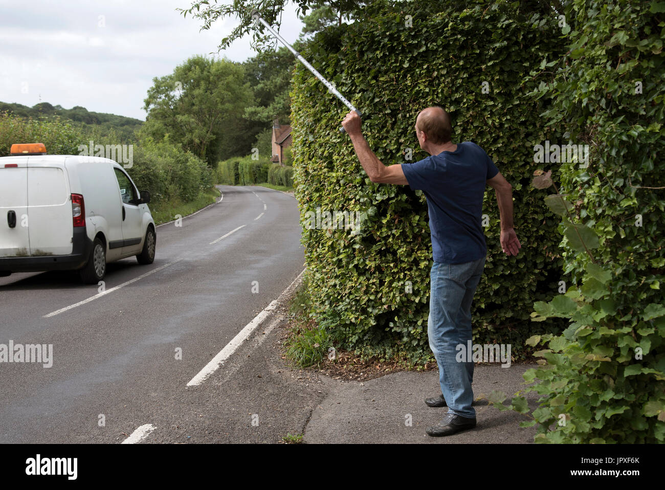 Angry elderly man trying to cross a road waving his walking stick at a passing motorist driving a white van Stock Photo