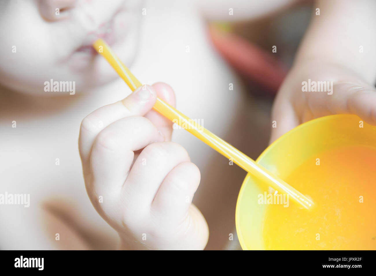 Drinking some fresh orange from a yellow plastic glass using a straw. Top view. Stock Photo