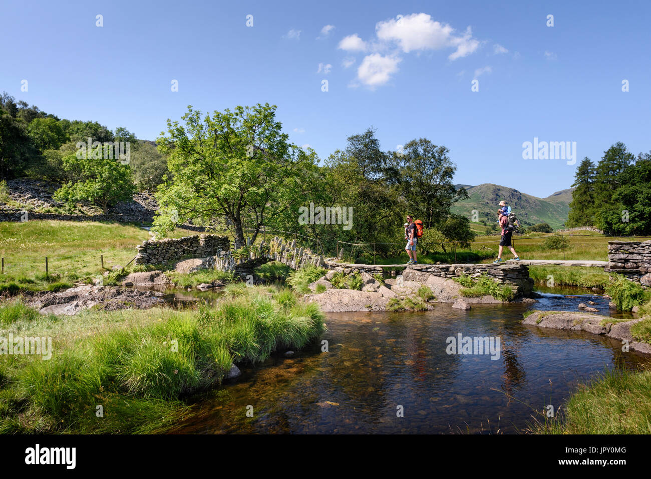 Two fathers carrying children in baby carriers over Slater's Bridge & River Brathay in Little Langdale in the English Lake District, Cumbria Stock Photo