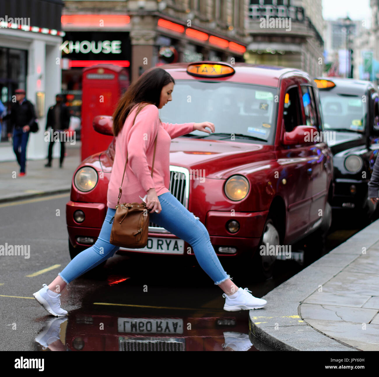 Woman stepping over puddle infront of Taxi's in London Stock Photo