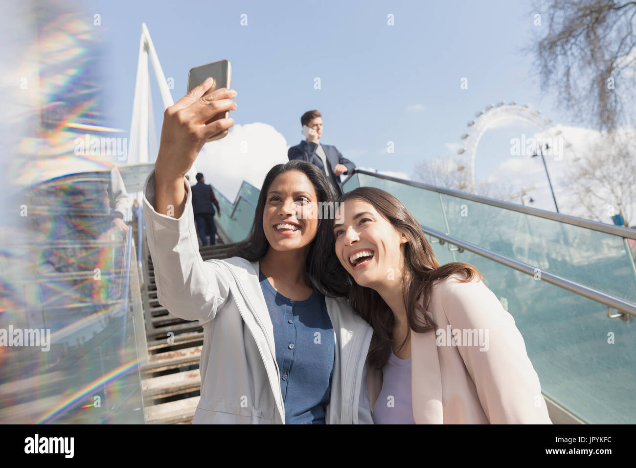 Enthusiastic, smiling women friends taking selfie with camera phone on sunny, urban stairs, London, UK Stock Photo