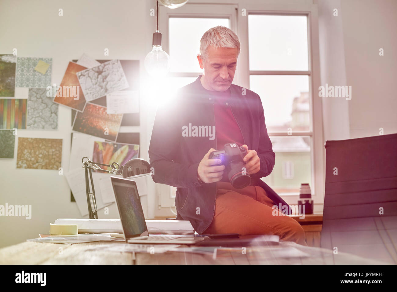 Male photographer using digital camera in sunny office Stock Photo