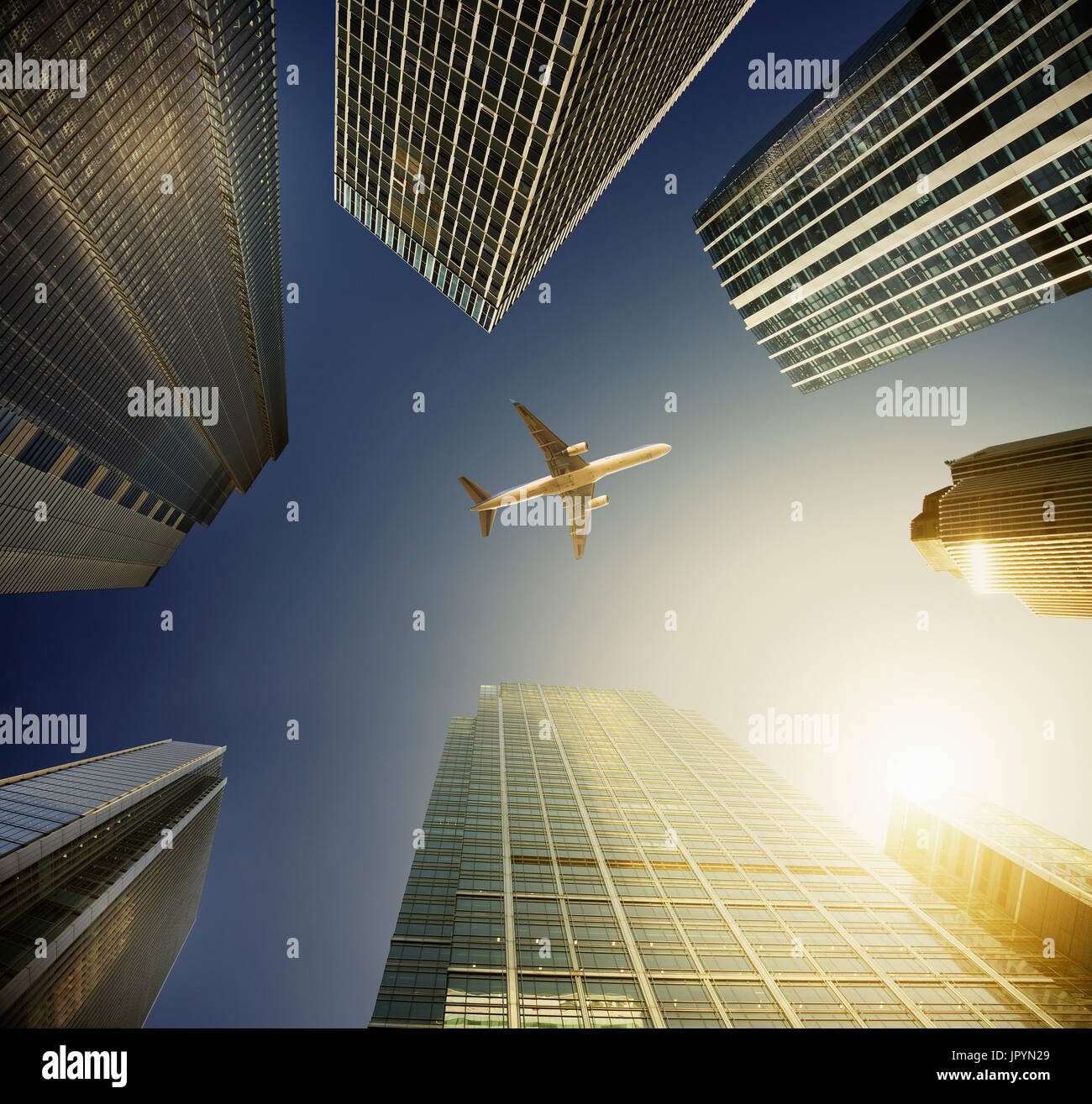 Airplane flying in blue sky over highrise buildings, travel concept Stock Photo