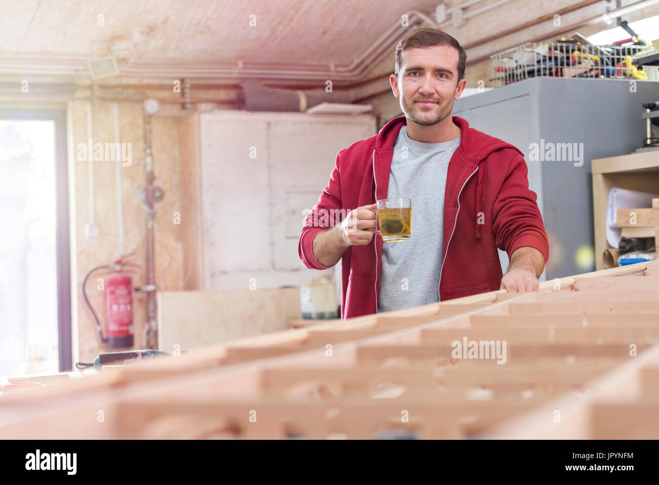 Portrait confident male carpenter drinking tea at wood boat in workshop Stock Photo