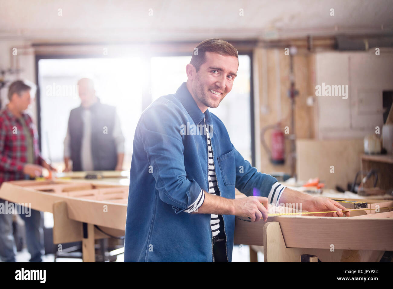 Portrait smiling male carpenter measuring wood on boat in workshop Stock Photo