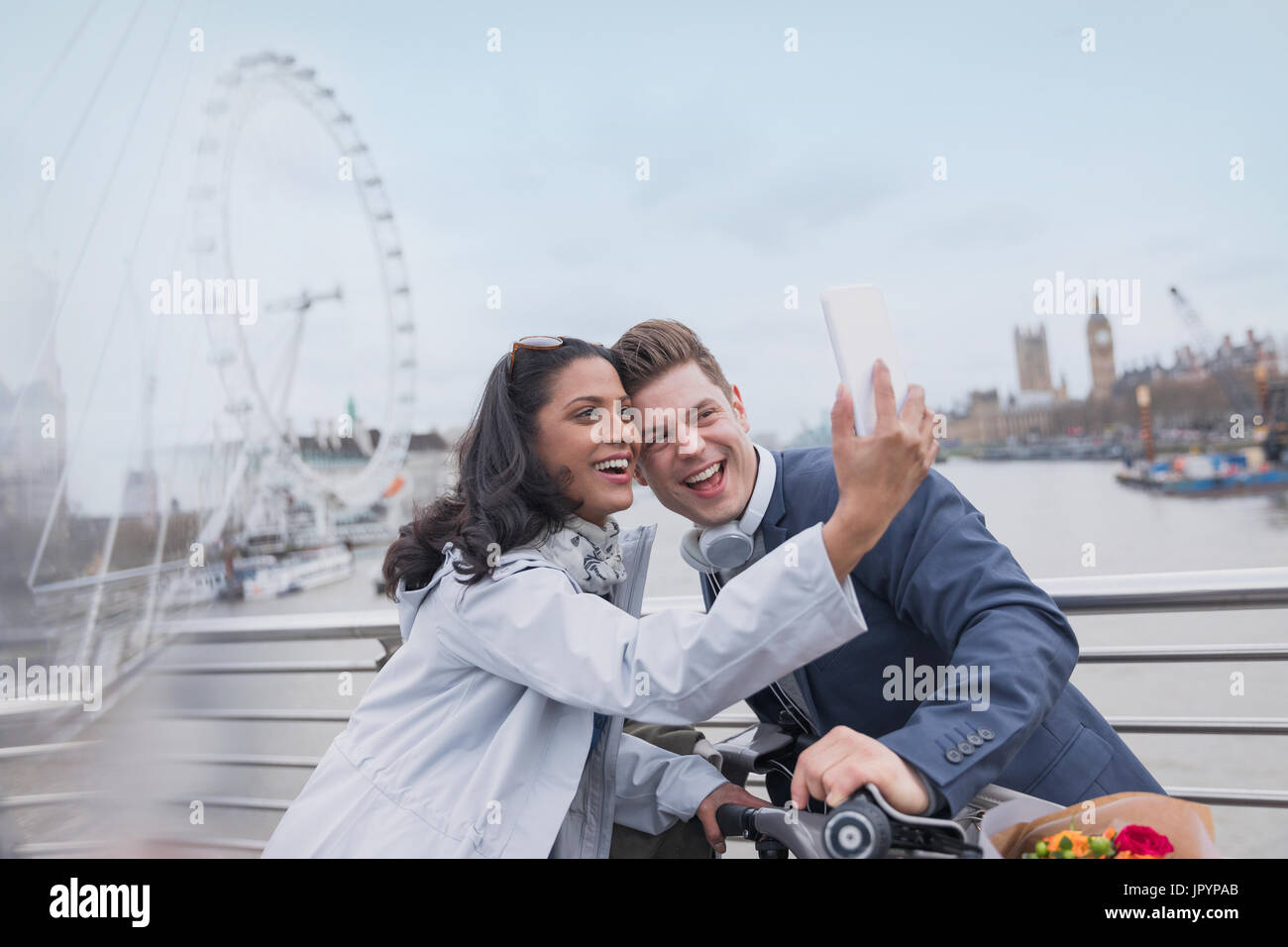 Smiling couple tourists taking selfie with camera phone on bridge near Millennium Wheel, London, UK Stock Photo