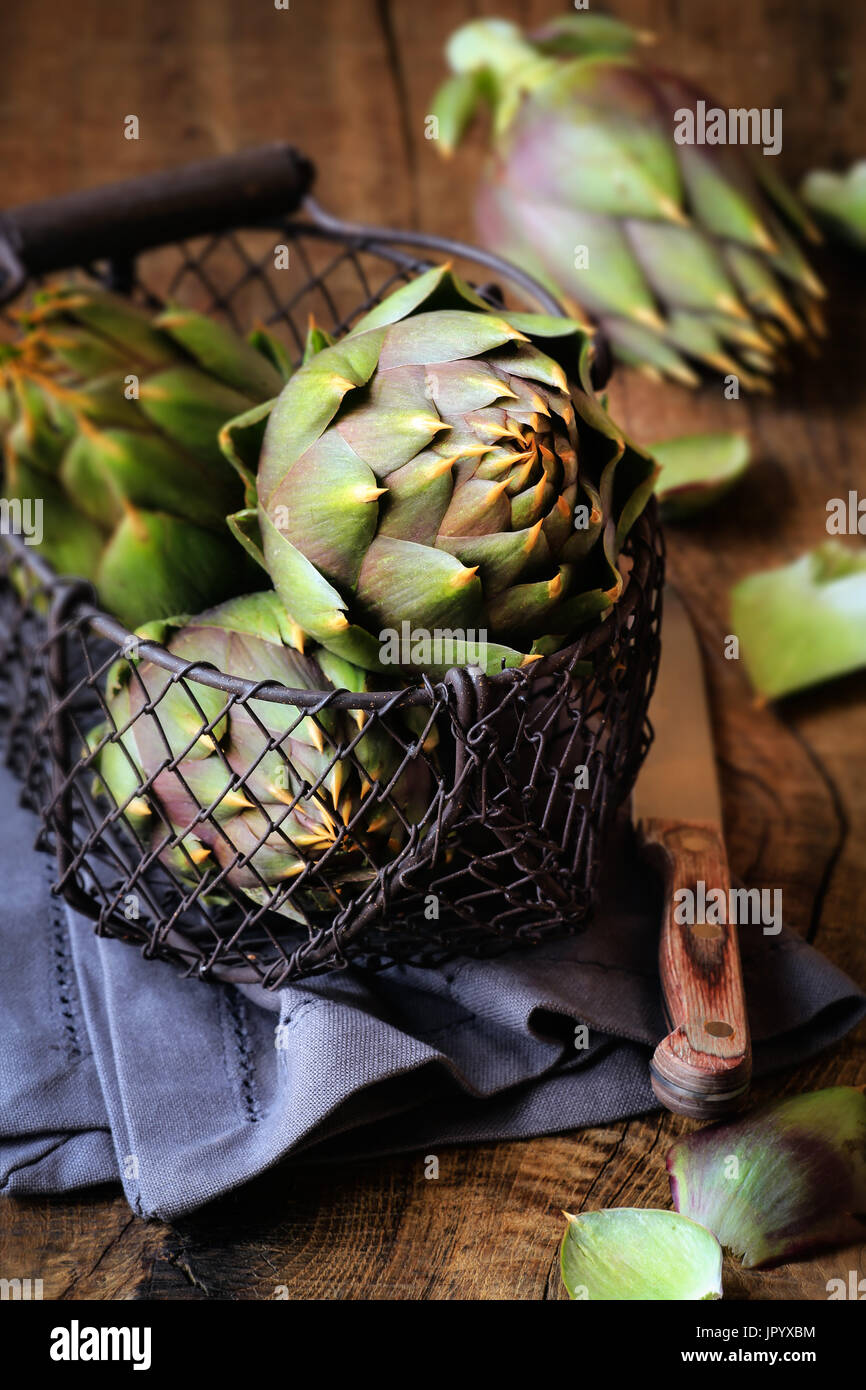 Sardinian thorny artichokes in a wire basket on dark rustic wooden background Stock Photo