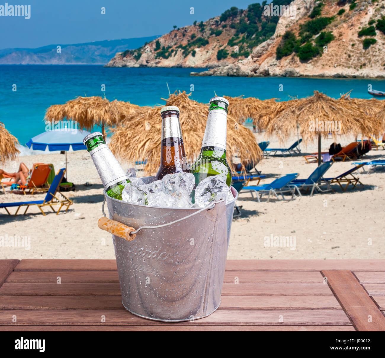 Three unopened bottles of beer inside ice bucket on beach background