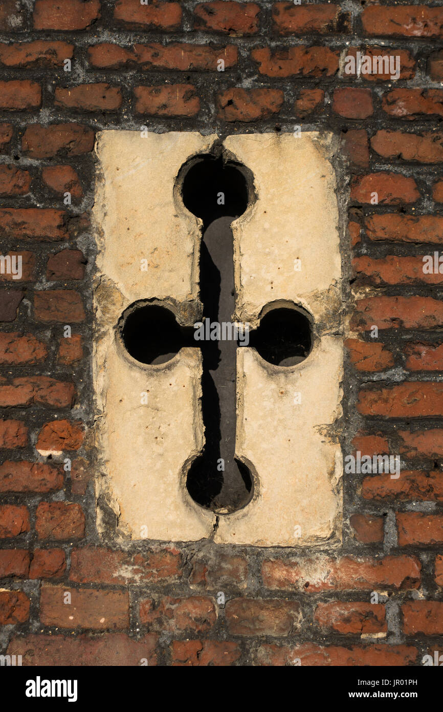 Close-up detail of cross-shaped window arrow slit in Tudor architecture exterior red brick wall Stock Photo
