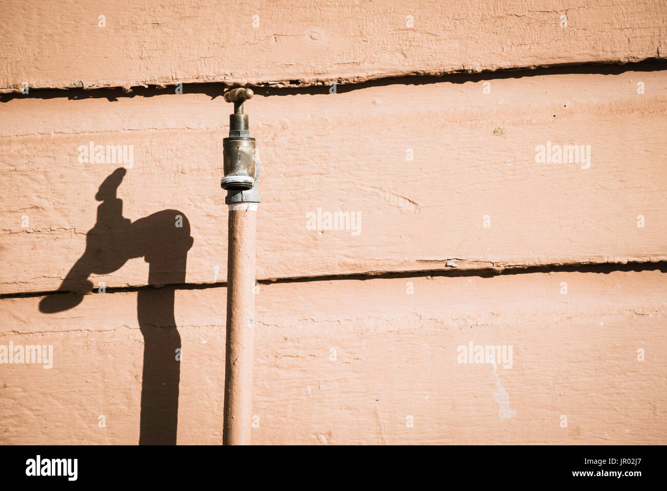 A single spigot or tap or faucet up against a timber wall in direct