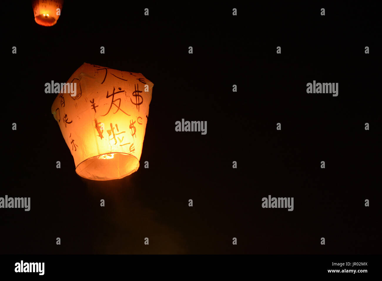 Sky lantern floating into the night sky at the festival in Pingxi, the Chinese text is a wish for money in the New Year Stock Photo