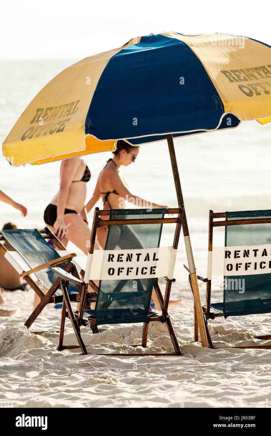 Lounge chairs and umbrella on the beach. Women in bikinis walking by in the background. Stock Photo