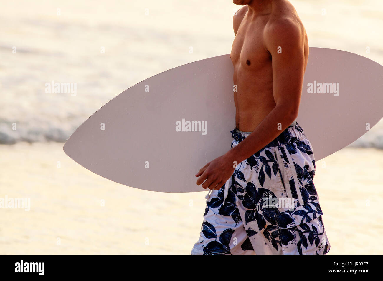 Young man carrying a skim board walking on a beach. Panama City Beach