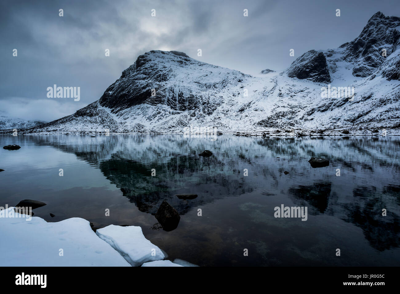 Landscape Of Rugged, Snow Covered Mountains Reflected In Tranquil Ocean Water; Lofoton Islands, Nordland, Norway Stock Photo