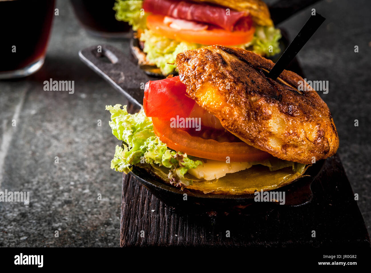 Mexican Tortilla de patatas rellena de jamón serrano - casserole with potato, eggs, sandwich with meat, lettuce, cheese, tomatoes. In portioned frying Stock Photo