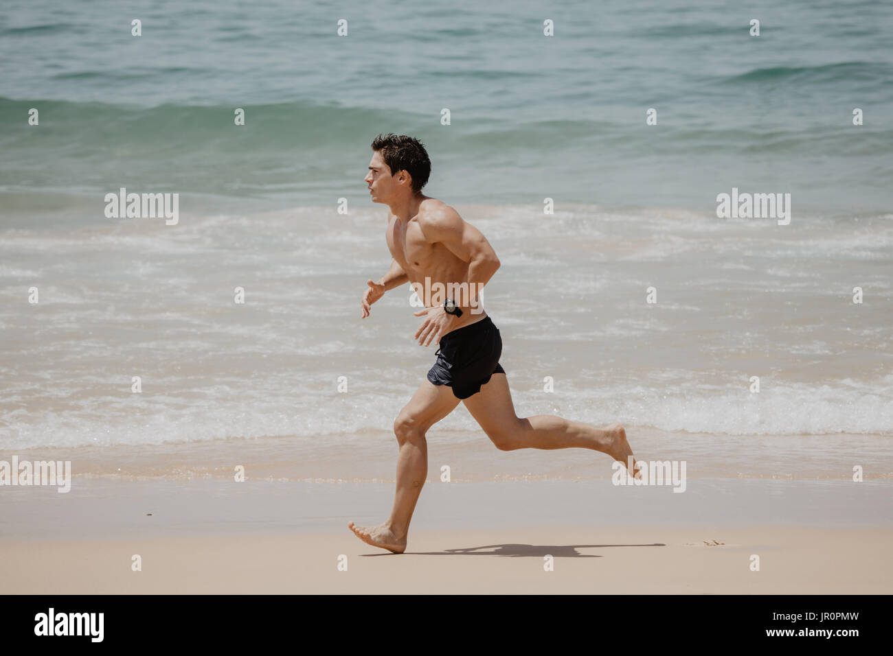 Young Man In Fitness Clothing Running Along Beach Stock Photo