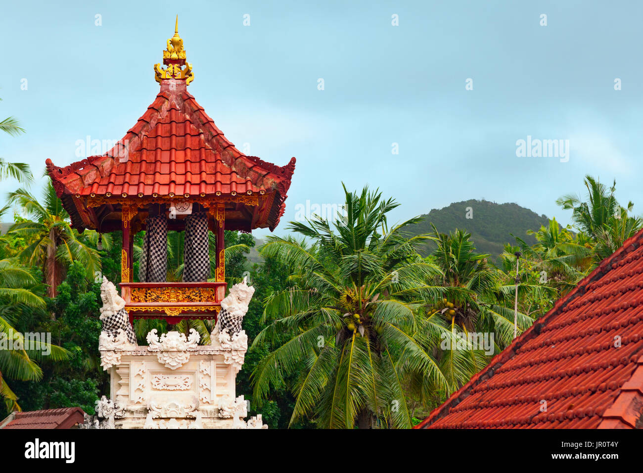 Wooden bells kulkul on traditional belfry with carving on white limestone walls. Balinese hindu temple on jungle and rainy sky background. Nusa Penida Stock Photo