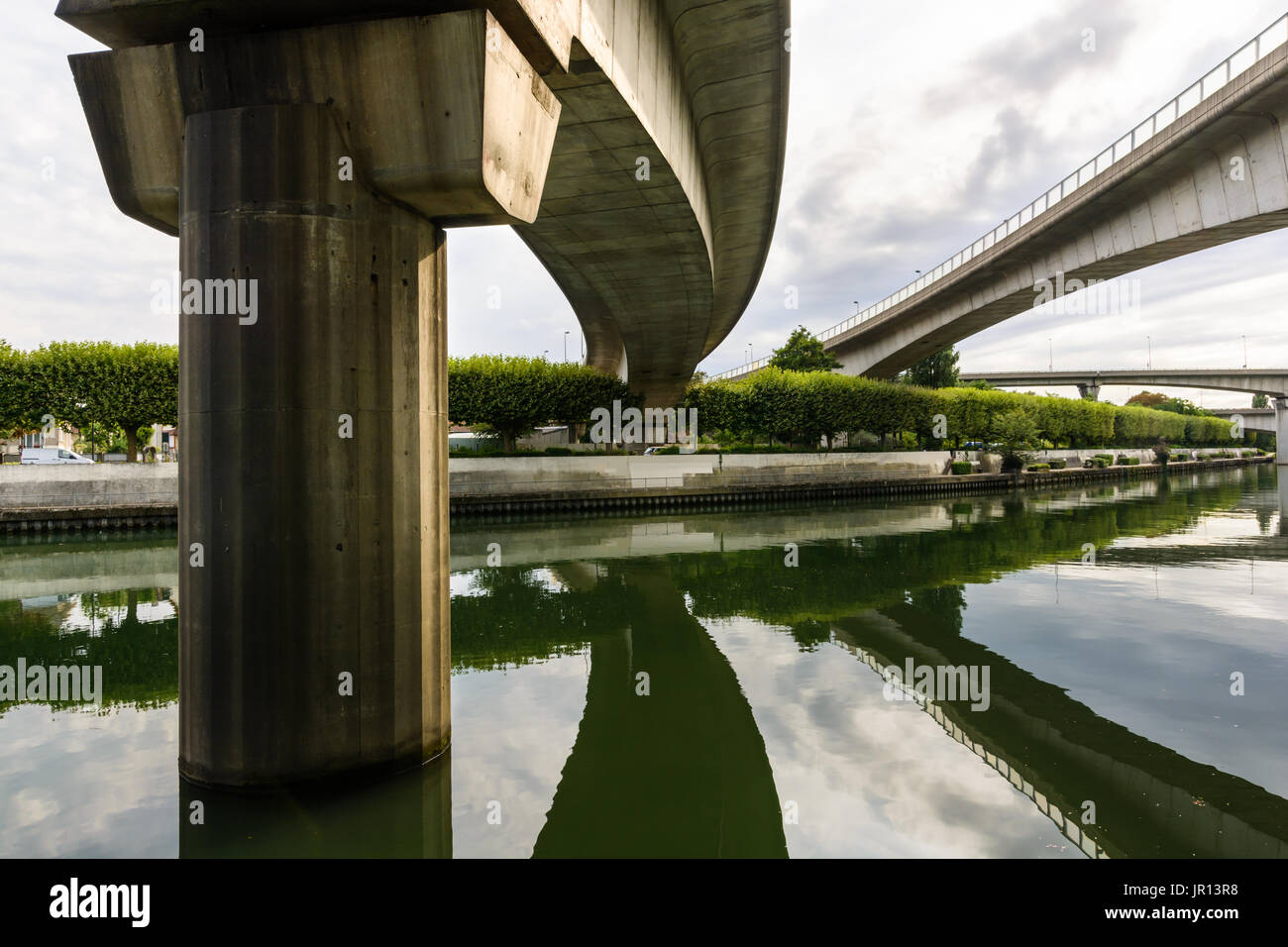Highway junctions spanning and reflecting in the still waters of the river Marne under a cloudy sky. Stock Photo