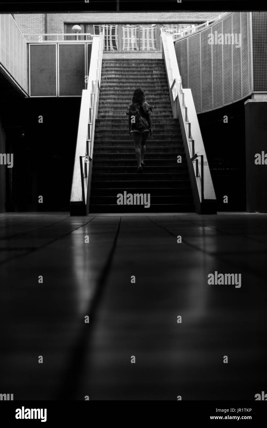 Black and white photograph of a black silhouette of a girl walking towards a few stairs in the city. Stock Photo