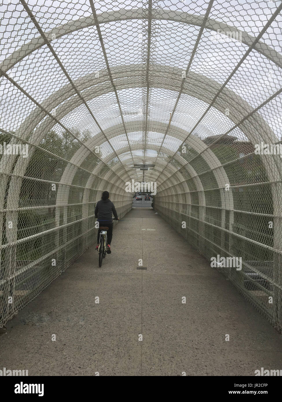 Girl in black rides a bike in a tunnel over a highway in Brooklyn New York. Alternative transportation to cars, riding a bike city on a gloomy day in  Stock Photo