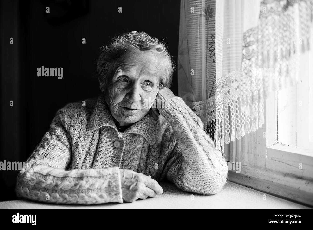 An elderly woman sitting at the table, a black-and-white photograph. Stock Photo