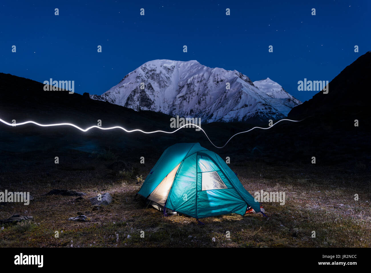 Nighttime View Of Mt. Moffit With A Lit Tent And Headlamp Trail In The Foreground, Alaska Range, Interior Alaska, USA Stock Photo